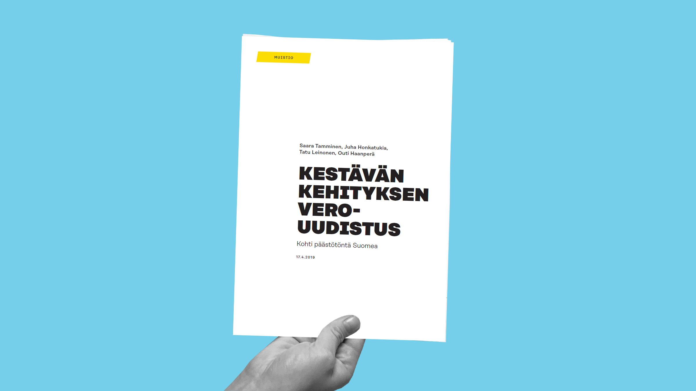 Kädessä on kestävän kehityksen verouudistus -kirjanen, jonka otsikon yläpuolella on kirjoittajien nimet sinisellä pohjalla. Pääosin valkoisessa vihkosessa on lihavoitu musta teksti ja pieni keltainen etiketti nurkassa.
