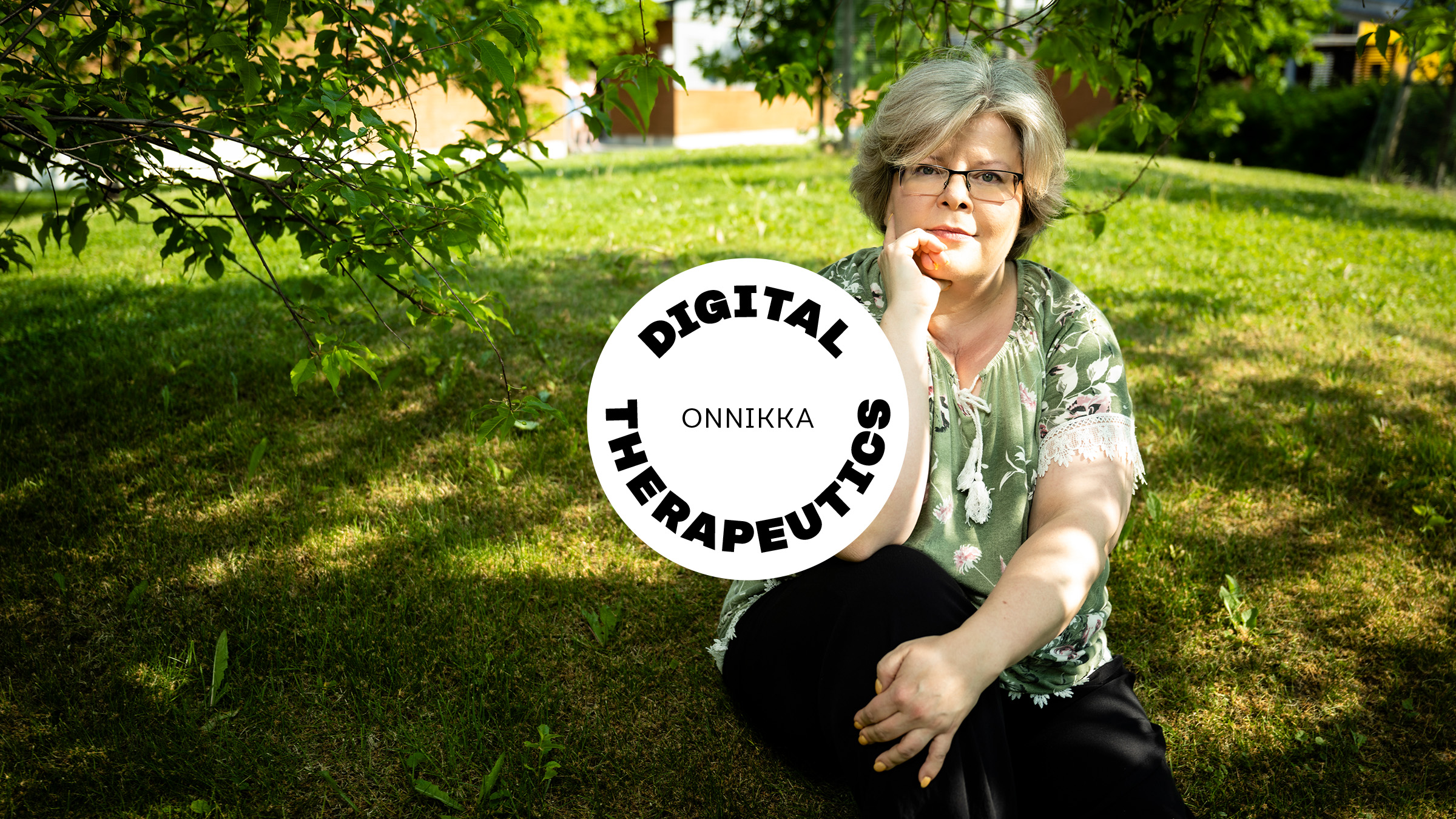 Tarja Viitanen sits on the lawn, with a building and trees in the background. On top is a sticker that says digital therapeutics.s.